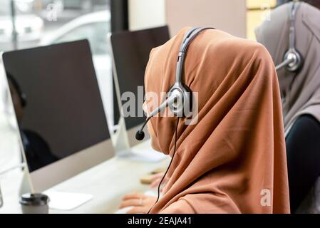 Vue arrière d'une femme d'affaires musulmane portant un micro-casque avec lequel elle travaille équipe au bureau du centre d'appels Banque D'Images