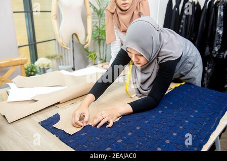 Femme musulmane designer de mode épinglant le motif de papier sur le tissu à la table dans son magasin de tailleur Banque D'Images