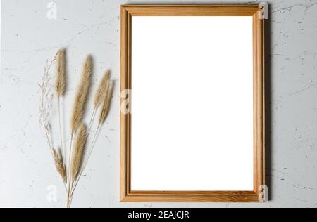 Maquette. Un cadre photo en bois sur un mur texturé avec des tiges d'herbe sèche et moelleuse. Banque D'Images