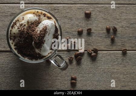 Tasse de café en verre avec lait, crème glacée et chocolat râpé sur une surface en bois avec grains de café rôtis. Mise au point sélective. Banque D'Images