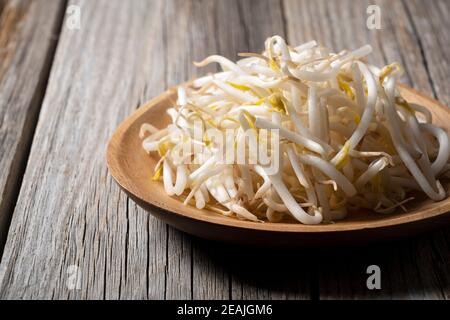 Le haricot s'élance dans une assiette en bois contre un ancien arrière-plan en bois Banque D'Images
