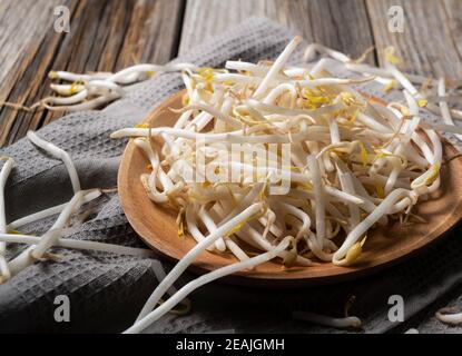 Le haricot s'élance dans une assiette en bois contre un ancien arrière-plan en bois Banque D'Images