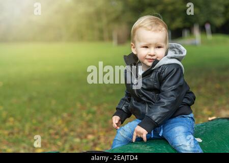 Un petit garçon vêtu d'une veste en cuir pose à l'extérieur Banque D'Images