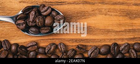 Grains de café avec une cuillère en gros plan éparpillés sur une table en bois texturé. Banque D'Images