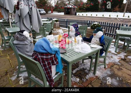 Ashford, Kent, Royaume-Uni. 10 février 2021. Forcés de fermer en raison de la pandémie, les Chequers sur le pub Green sur l'A28 Ashford Rd à High Halden ont mis au point une nouvelle façon d'amuser les passants avec la neige arrivant de Storm Darcy. Une famille de figures de neige s'assoient à l'extérieur en buvant et en mangeant. Crédit photo : Paul Lawrenson/Alay Live News Banque D'Images