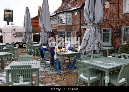 Ashford, Kent, Royaume-Uni. 10 février 2021. Forcés de fermer en raison de la pandémie, les Chequers sur le pub Green sur l'A28 Ashford Rd à High Halden ont mis au point une nouvelle façon d'amuser les passants avec la neige arrivant de Storm Darcy. Une famille de figures de neige s'assoient à l'extérieur en buvant et en mangeant. Crédit photo : Paul Lawrenson/Alay Live News Banque D'Images