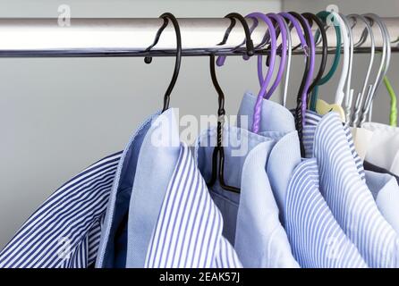 Ensemble de chemises à rayures bleu clair accrochées à la tige d'une garde-robe blanche. Banque D'Images