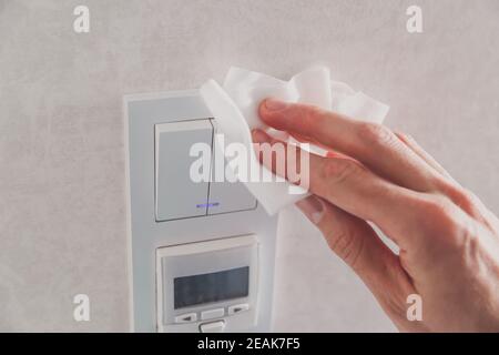 Prévenir les infections et les virus, nettoyer le commutateur d'éclairage de la cuisine à la maison avec un chiffon désinfectant blanc. Coronavirus COVID-19. Banque D'Images