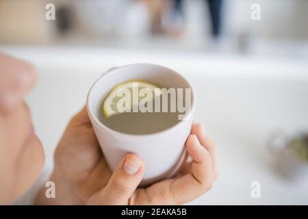 Femme soufflant doucement sur une tasse de thé de citron avec une tranche de citron à l'intérieur Banque D'Images