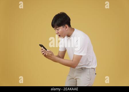 portrait de choqué surpris excité jeune asiatique habillé à la mode je regarde le smartphone mobile isolé sur fond jaune de studio Banque D'Images