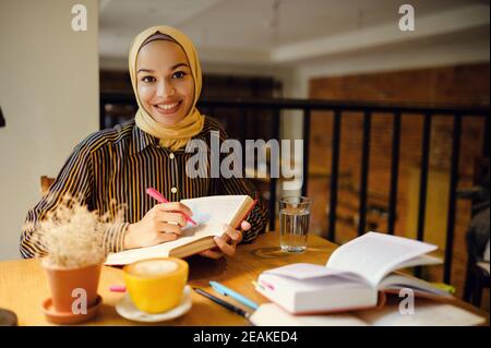 Une jeune fille arabe souriante dans le hijab tient un carnet Banque D'Images