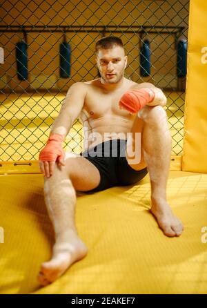 Un combattant MMA mâle assis sur le sol dans une cage Banque D'Images