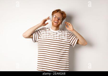 Concept de technologie. Heureux redhead homme écoutant de la musique dans les écouteurs et chantant le long, debout sur fond blanc Banque D'Images