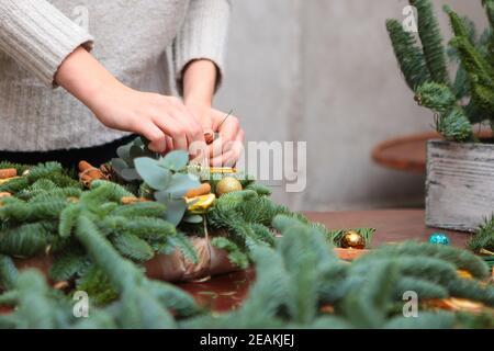 La jeune fille fait ses mains une couronne de Noël de branches d'épinette et d'eucalyptus danois. Décoration traditionnelle pour le nouvel an ou Noël. Photo sans visages, mains seulement. Banque D'Images