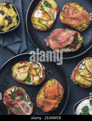 Bruschetta assorti avec différentes garnitures sur des assiettes sombres sur fond sombre. La bruschetta appétissante. Cuisine méditerranéenne. Vue de dessus Banque D'Images