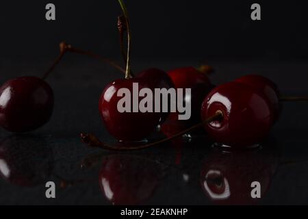Cerises, avec des gouttes d'eau sur un fond noir avec réflexion Banque D'Images