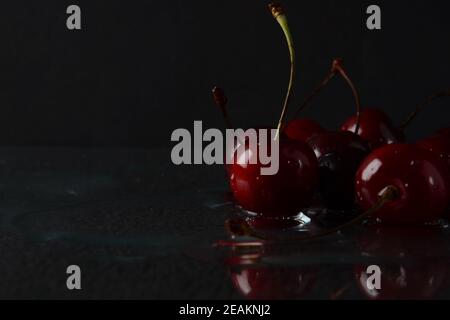 Cerises, avec des gouttes d'eau sur un fond noir avec réflexion Banque D'Images