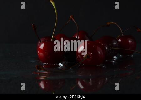 Cerises, avec des gouttes d'eau sur un fond noir avec réflexion Banque D'Images