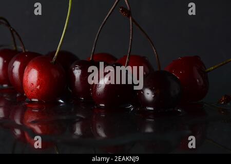 Cerises, avec des gouttes d'eau sur un fond noir avec réflexion Banque D'Images