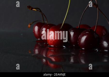 Cerises, avec des gouttes d'eau sur un fond noir avec réflexion Banque D'Images