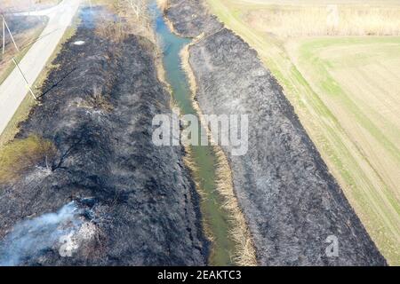 Brûlage d'herbe sèche le long du canal d'irrigation. La fumée et le flam Banque D'Images