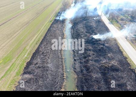 Brûlage d'herbe sèche le long du canal d'irrigation. La fumée et le flam Banque D'Images
