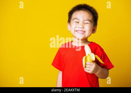 enfant mignon petit garçon sourire attrayant portant t-shirt rouge jouer contient la banane pelée pour manger Banque D'Images