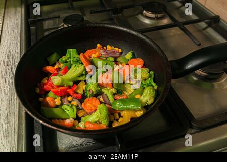 Beaucoup de légumes colorés sont frits dans une poêle de la cuisine. Carottes, poivrons, brocoli, pisums, pois, maïs et oignons Banque D'Images