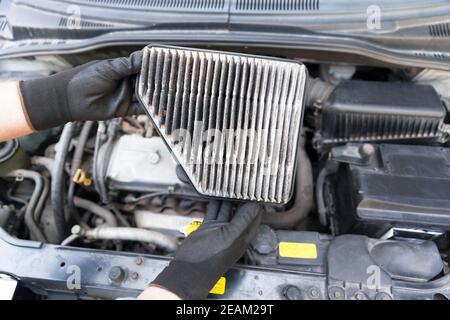 Auto mécanicien portant des gants de protection pour le travail et tenant le filtre à air sale au-dessus d'un moteur de voiture Banque D'Images