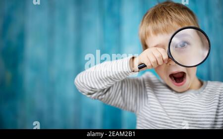 Un petit garçon choqué de regarder à travers une loupe Banque D'Images