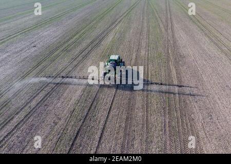 Tracteur avec système de pulvérisation de pesticides sur charnières. Fertilisation avec un tracteur, sous forme d'aérosol, sur le champ de blé d'hiver. Banque D'Images