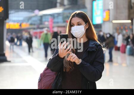 Fille étudiante portant un masque de protection acheter un billet en ligne avec un smartphone à la gare Banque D'Images