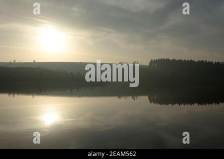 Lumière du soleil lumineuse, faible dans le ciel, reflétée de façon floue dans l'eau Banque D'Images