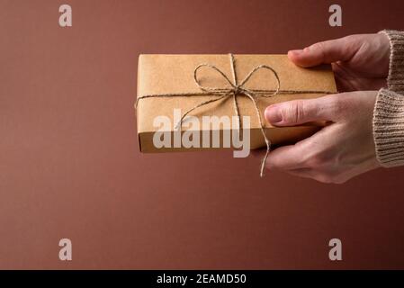 Boîte-cadeau simple en papier avec noeud de ficelle dans les mains de femme sur marron Banque D'Images