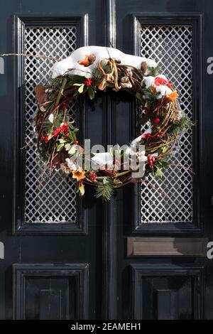 Une couronne de Noël enneigée est suspendue à une porte avant décorée d'une maison à IJlst, Frise, en hiver. Image verticale Banque D'Images