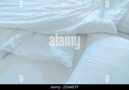 Lit confortable blanc et oreiller moelleux dans une chambre moderne. Couverture en lin blanc dans la chambre d'hôtel. Gros plan sur une couverture blanche désordonnée après le réveil. Lit confortable avec couette blanche douce. Banque D'Images