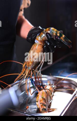 Le chef tient une crevette géante d'eau douce dans sa main. Personne méconnaissable. Mains dans des gants de protection. Concept de cuisine. Banque D'Images