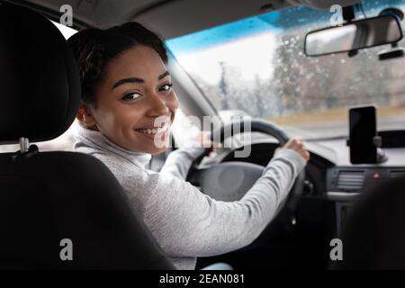 Une femme dans une voiture intérieure garde le volant, tourne autour, parle avec le passager du client dans le siège arrière Banque D'Images