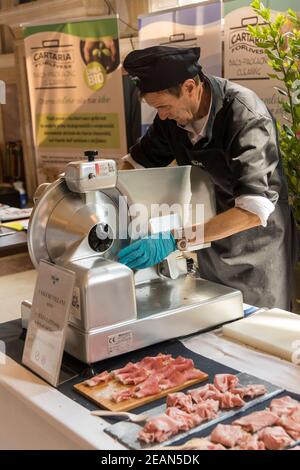Un homme qui coupe de la viande et du jambon de parme sur une publicité Machine à trancher lors d'un événement alimentaire à Bologne, Italie Banque D'Images