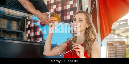 Belle femme qui a un hamburger comme plats à emporter de la cuisine dans un camion alimentaire Banque D'Images