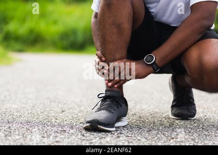 sport coureur homme utiliser les mains joint tenir la douleur de jambe parce que de la cheville tordue brisée pendant la course Banque D'Images