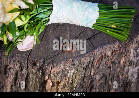 Deux magnifiques anneaux de mariage sur une souche en bois et un morceau du bouquet Banque D'Images