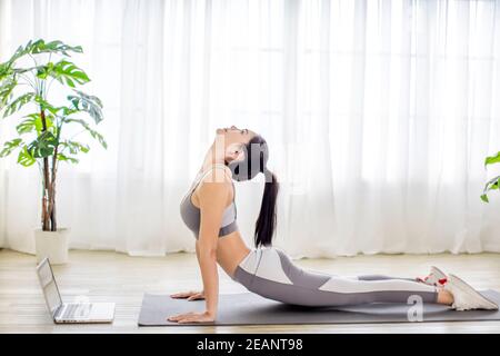 Jeune femme en vêtements de sport regardant la vidéo en ligne avec des exercices de forme physique sur ordinateur portable Banque D'Images