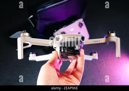 Kiev, Ukraine - 02 février 2021: DJI Mavic Mini 2 gros plan de drone. Main tenant le quadricoptère déplié avec télécommande sur fond noir en violet Banque D'Images