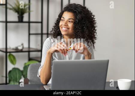 Jolie charmante jeune femme afro-américaine avec une coiffure afro-américaine assise au bureau et regardant dans la fenêtre, prenant une pause de travail sur un Banque D'Images