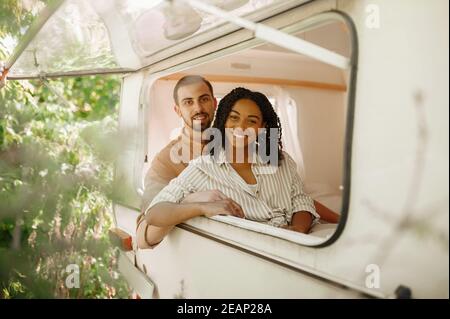 Le couple regarde par la fenêtre du véhicule de camping, campant dans la remorque Banque D'Images