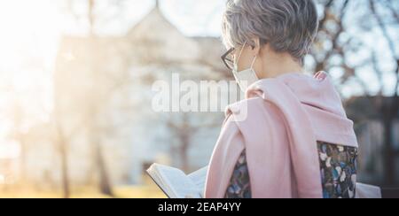 Dame senior avec masque de visage lisant la bible devant une église Banque D'Images