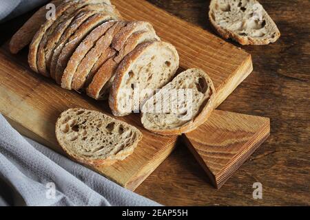 Pain ciabatta fraîchement cuit coupé en tranches sur une planche à découper en bois avec couteau Banque D'Images