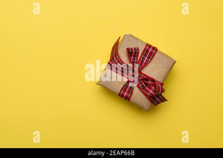 boîte carrée avec un cadeau enveloppé dans du papier brun et attaché avec un ruban rouge de soie Banque D'Images