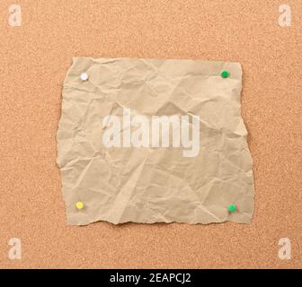 morceau de papier déchiré marron épinglé avec boutons de fer sur un panneau en liège brun Banque D'Images